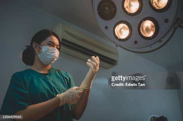 an asian chinese female surgeon getting ready and putting her surgical gloves on in the operating room illumined by surgical light - putting gloves stock pictures, royalty-free photos & images
