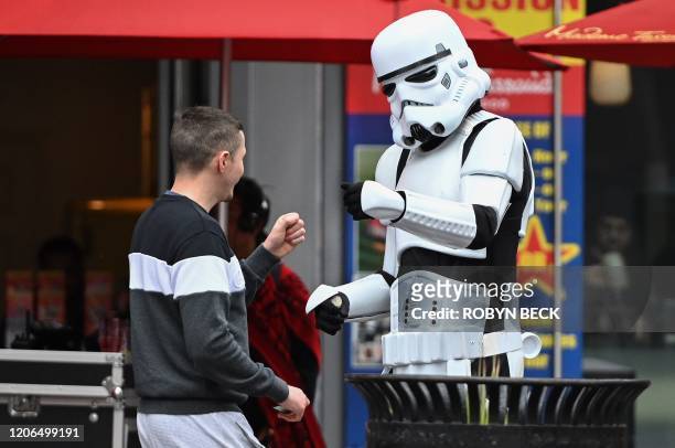 Person in a Stormtrooper costume who poses for snapshots with tourists in exchange for tips fist bumps with a passerby, on the Hollywood Boulevard in...