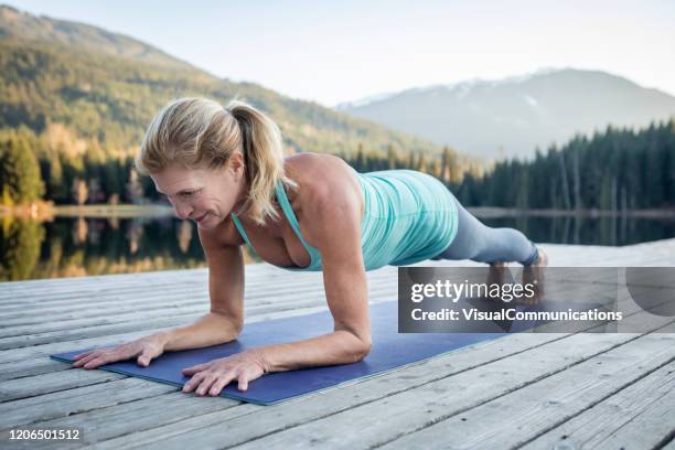 mujer mayor haciendo tablones en el muelle cerca del lago durante la puesta del sol. - postura de plancha fotografías e imágenes de stock