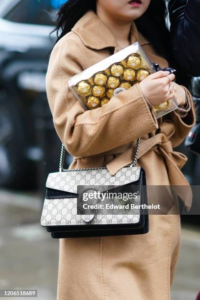 Guest wears a Gucci bag, a light brown coat and holds a Ferrero Rocher chocolate box, during London Fashion Week Fall Winter 2020, on February 15,...