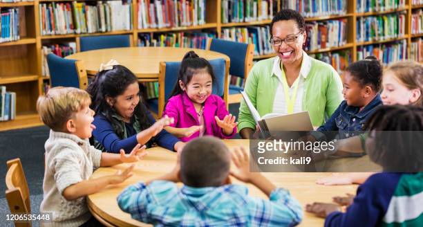 insegnante che legge ai bambini in biblioteca, gioca - bambini seduti in cerchio foto e immagini stock