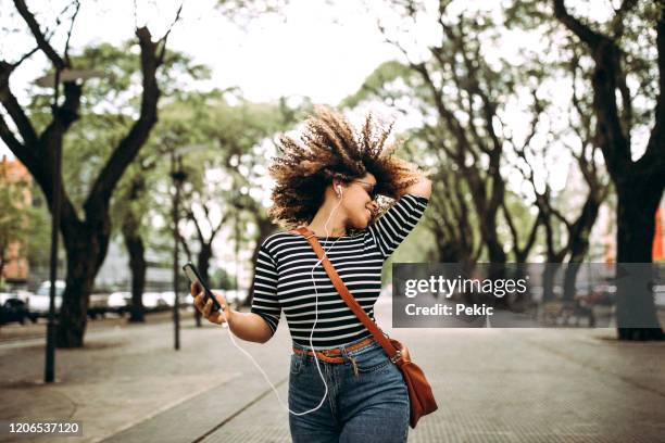 gelukkige spaanse vrouw die aan muziek luistert en op de straat danst - sing outside stockfoto's en -beelden