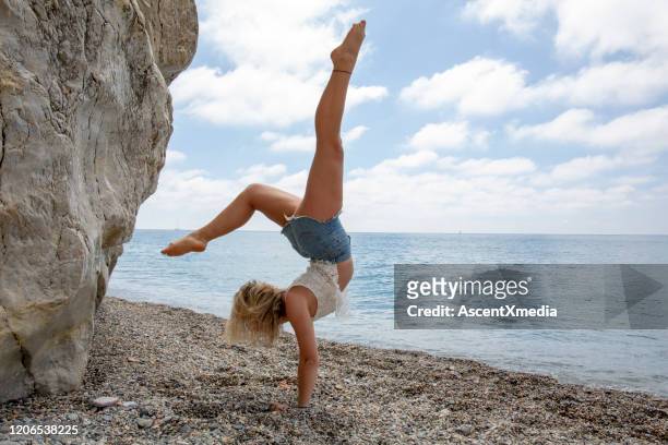 giovane donna pratica mosse yoga contro scogliera - blonde yoga foto e immagini stock