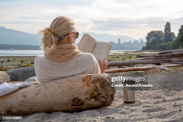 reife frau entspannt am strand bei sonnenaufgang - beach book reading stock-fotos und bilder