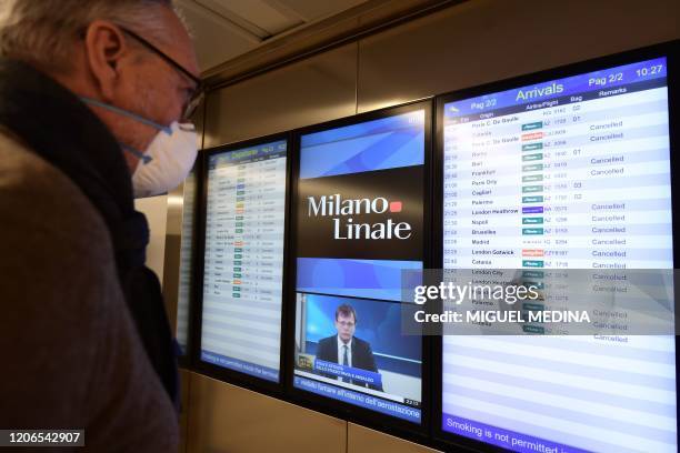 Passenger wearing a protective mask checks a flights timetable at Milan's Linate airport on March 11 a day after Italy imposed unprecedented national...