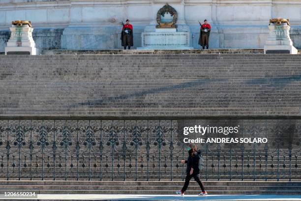 Person wearing a protective mask walks past guards in front of the closed Altare della Patria - Vittorio Emanuele II monument in central Rome on...