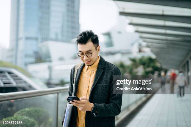 portrait of young urban asian businessman using smartphone and is carrying backpack on one shoulder while commuting in the city - hong kong advertising stock pictures, royalty-free photos & images