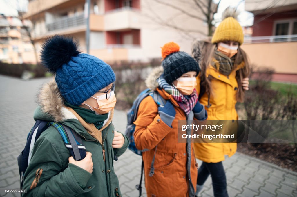 Drie jonge geitjes die antivirusmaskers dragen die naar school gaan