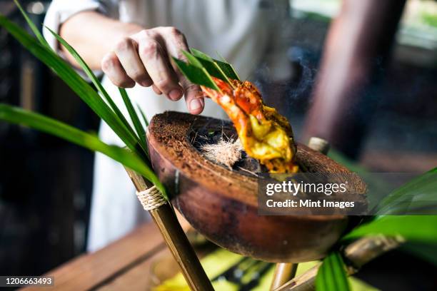 close up of chef preparing charcoal-grilled prawn satay on a coconut shell. - fusion food stock pictures, royalty-free photos & images