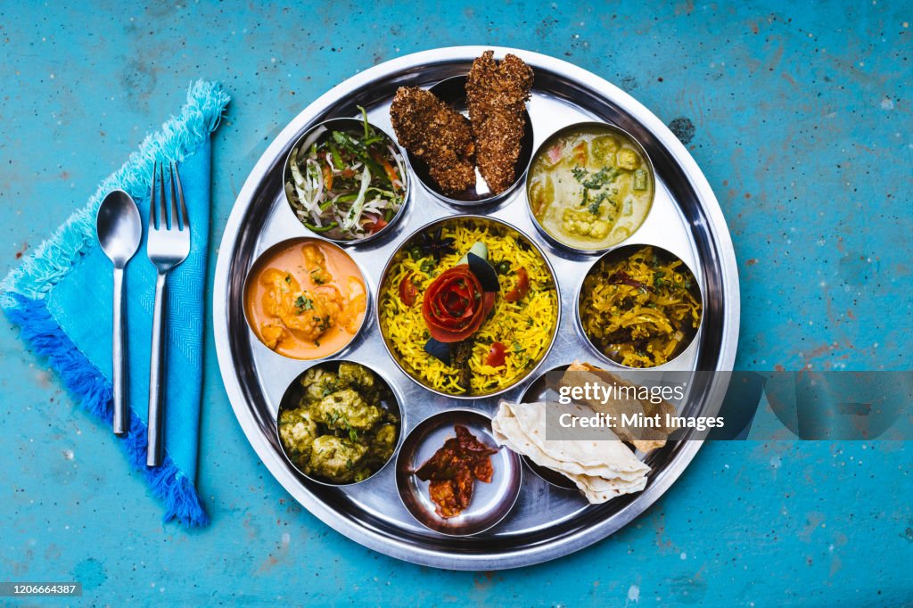 High angle close up of traditional Indian lunch with rice, various curries, pickles, and vegetables.