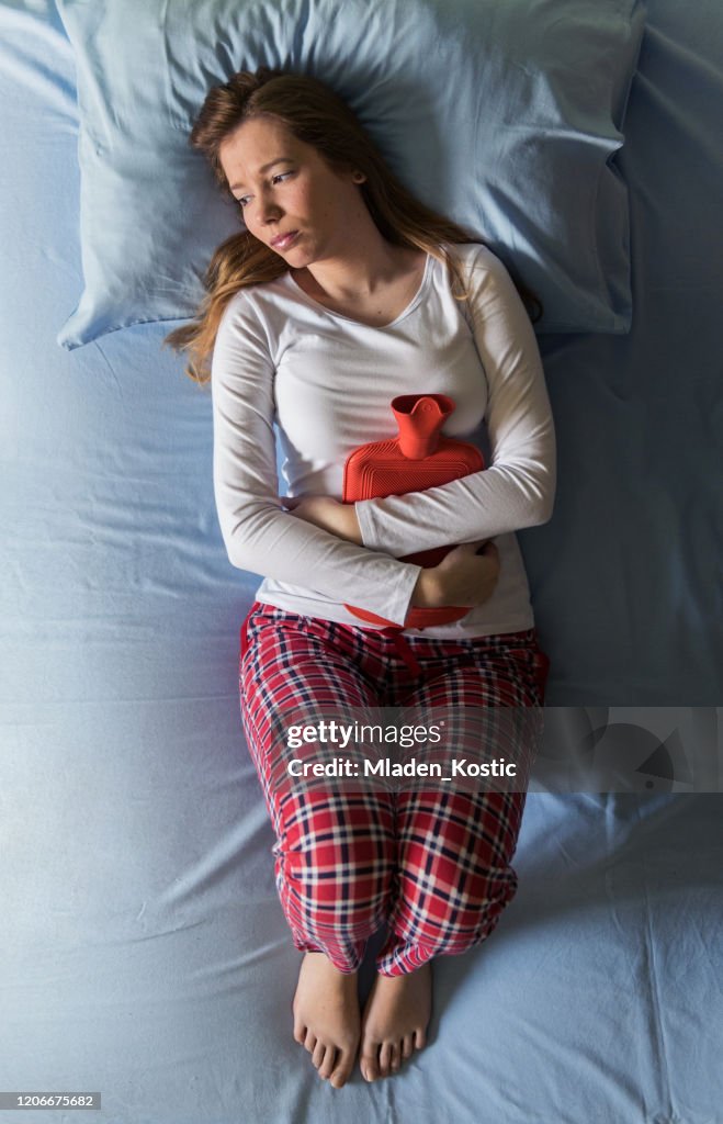 Jonge vrouw die in pijn, koude en griep, ziekte, pms, menstruatie ligt