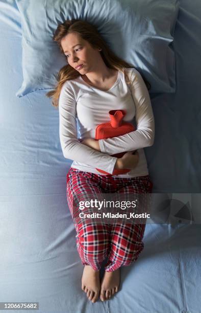 young woman lying in pain, cold and flu, illness, pms, menstruation - menstruation stock pictures, royalty-free photos & images