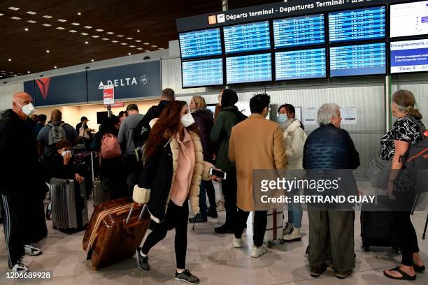 Traveller with a protective face mask pass by other standing in front of screens displaying departures flights at Paris-Charles-de-Gaulle airport...