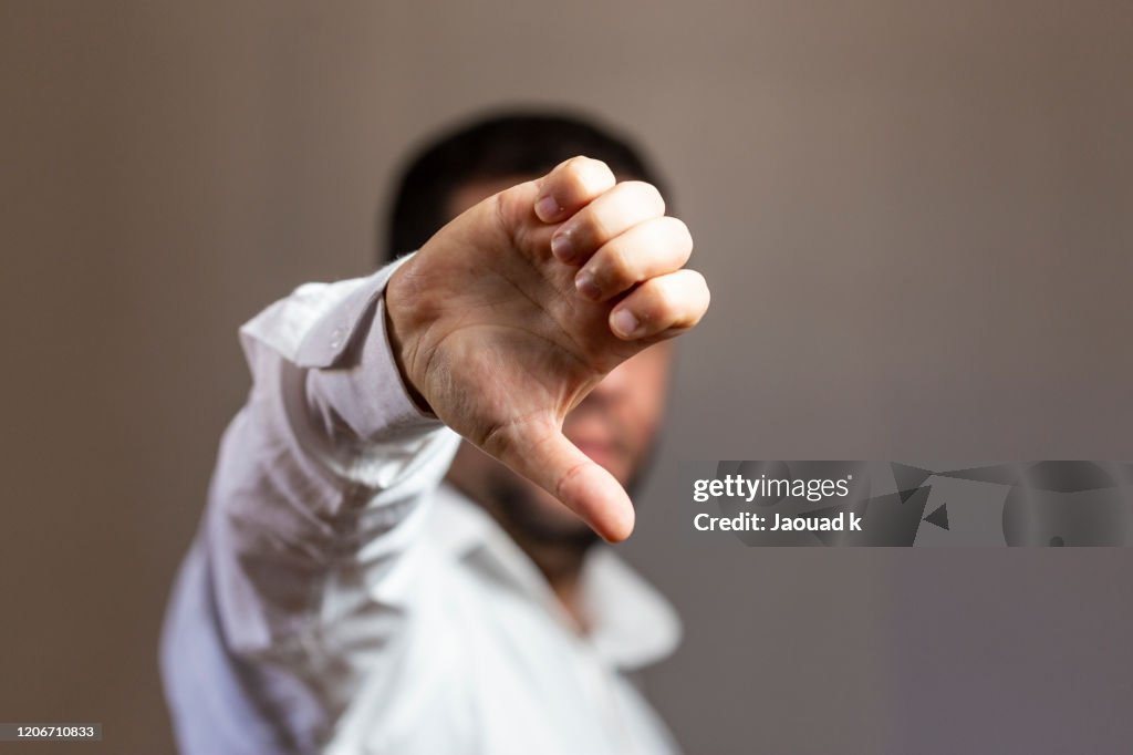 Man showing thumbs down sign , giving thumb down as sign of failure on gray background. customers feedback concept