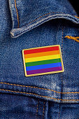 Gay pride flag pin on a denim jacket for LGBTQ identity, pride, and activism. The flag design is public domain for all uses.