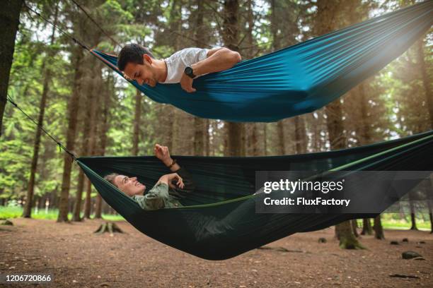 blissful couple talking while relaxing in hammocks - hammock camping stock pictures, royalty-free photos & images