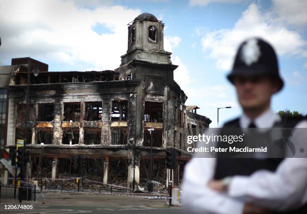 Police officer stands in front of a burnt out Carpetright shop in Tottenham on August 8, 2011 in London, England. Pockets of rioting and looting took...