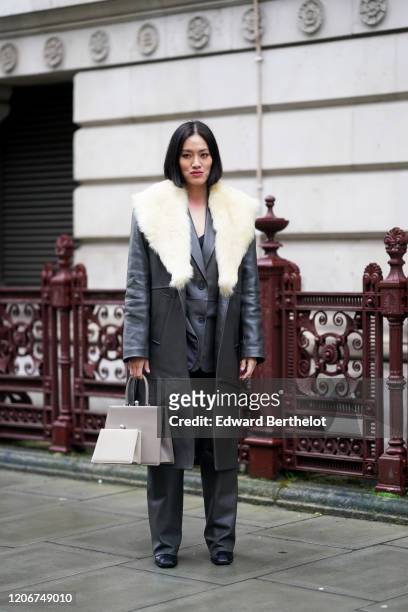 Tiffany Hsu wears a dark grau long leather coat with white faux fur, a gray double bag, flared pants, black shoes, during London Fashion Week Fall...