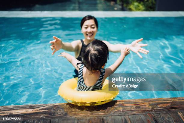 cute little asian toddler girl having fun and jumping into her mother's arms in the swimming pool in summer - hotel fun ストックフォトと画像