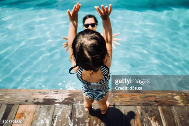 overhead view of little asian toddler girl having fun and jumping into her mother's arms in the swimming pool in summer - adult baby girl fotografías e imágenes de stock