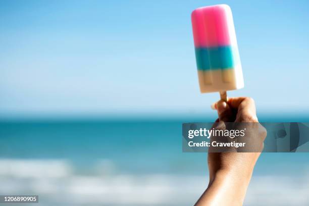 cropped image of woman's hand holding ice-cream by the sea against clear blue sky - eating dieting stock pictures, royalty-free photos & images