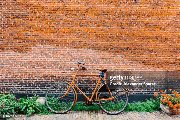 orange bicycle leaned on a brick wall - amsterdam cycling stock pictures, royalty-free photos & images