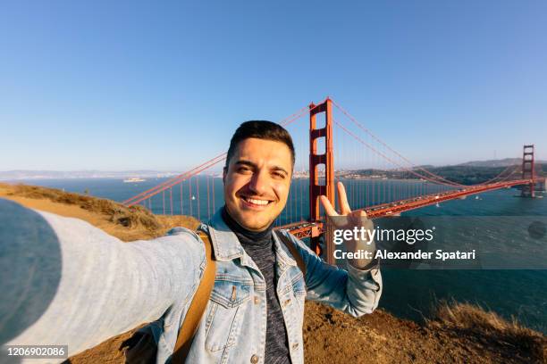 young smiling happy man taking selfie at golden gate bridge in san francisco, california, usa - autokorrekturfilter stock-fotos und bilder