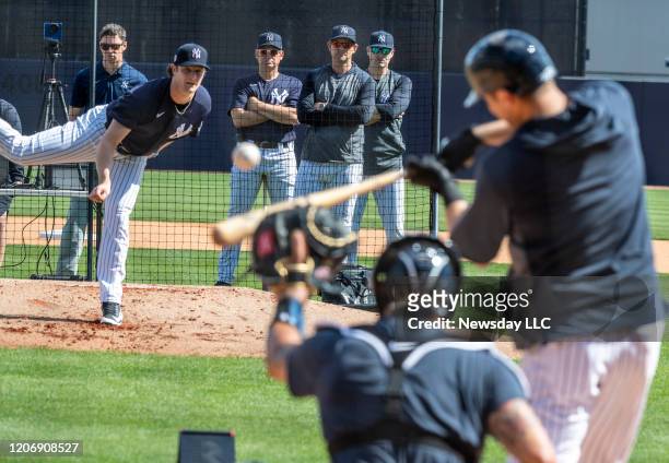 New York Yankees' pitcher Gerrit Cole pitching to batters from the mound with manager Aaron Boone, front center, bench coach Carlos Mendoza, left and...