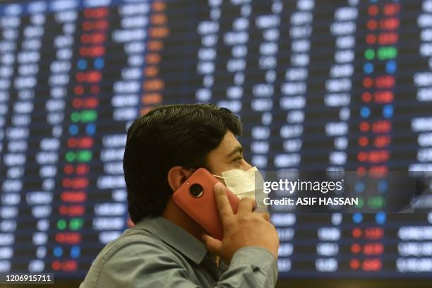 Stockbroker wearing a facemask amid concerns of the spread of the COVID-19 coronavirus, speaks on his cellphone as he watches share prices on a...