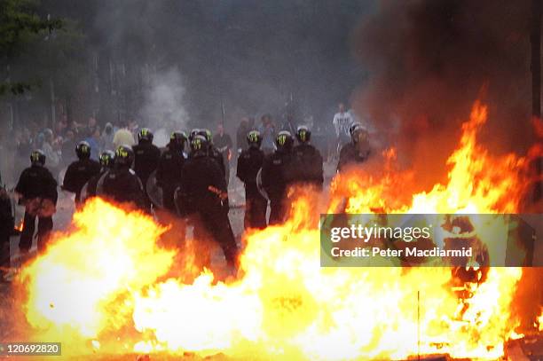 Police in riot gear stand near a burning car as it explodes in Hackney on August 8, 2011 in London, England. Pockets of rioting and looting continues...