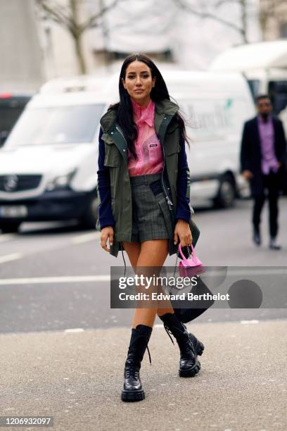 Tamara Kalinic wears a pink shirt, a green khaki coat, khaki checkered shorts, a pink mini Jacquemus bag, a Prada mini bag, black leather boots,...