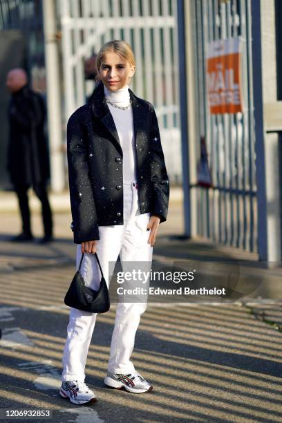 Caroline Daur wears a white turtleneck pullover, a chain necklace, a black oversized blazer jacket with flared sleeves and printed stars/dots, white...