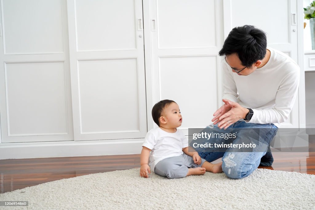 Happy Asian family of young father playing games and clapping hands with baby boy child at home
