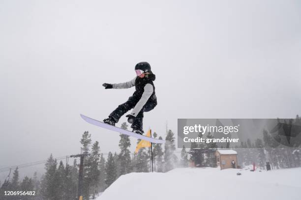 a young female snowboarder coming off a jump at a ski area in colorado on a snowy day - snowboard jump close up stock pictures, royalty-free photos & images