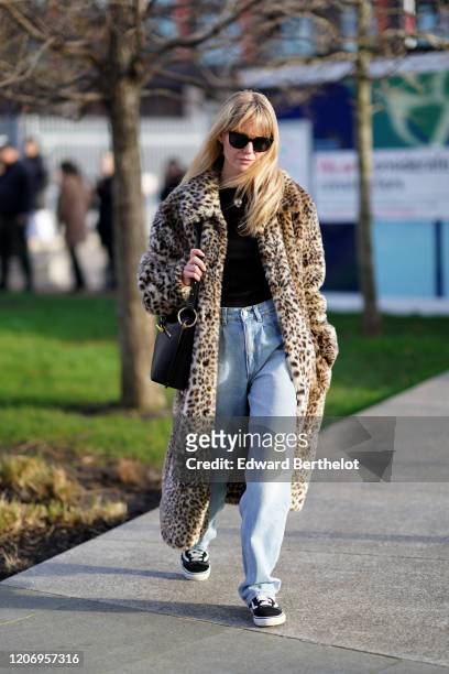 Jeanette Madsen wears sunglasses, a leopard print fluffy faux fur coat, a black top, blue denim jeans, a black leather bag, sneakers, during London...