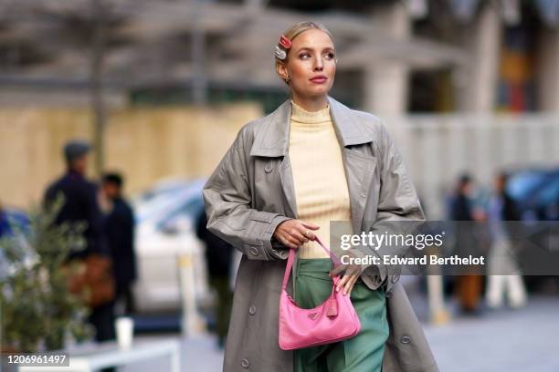 Leonie Hanne wears hair pins, a pale yellow pullover, a gray trench coat, green pants, a pink Prada fanny pack bag, during London Fashion Week...