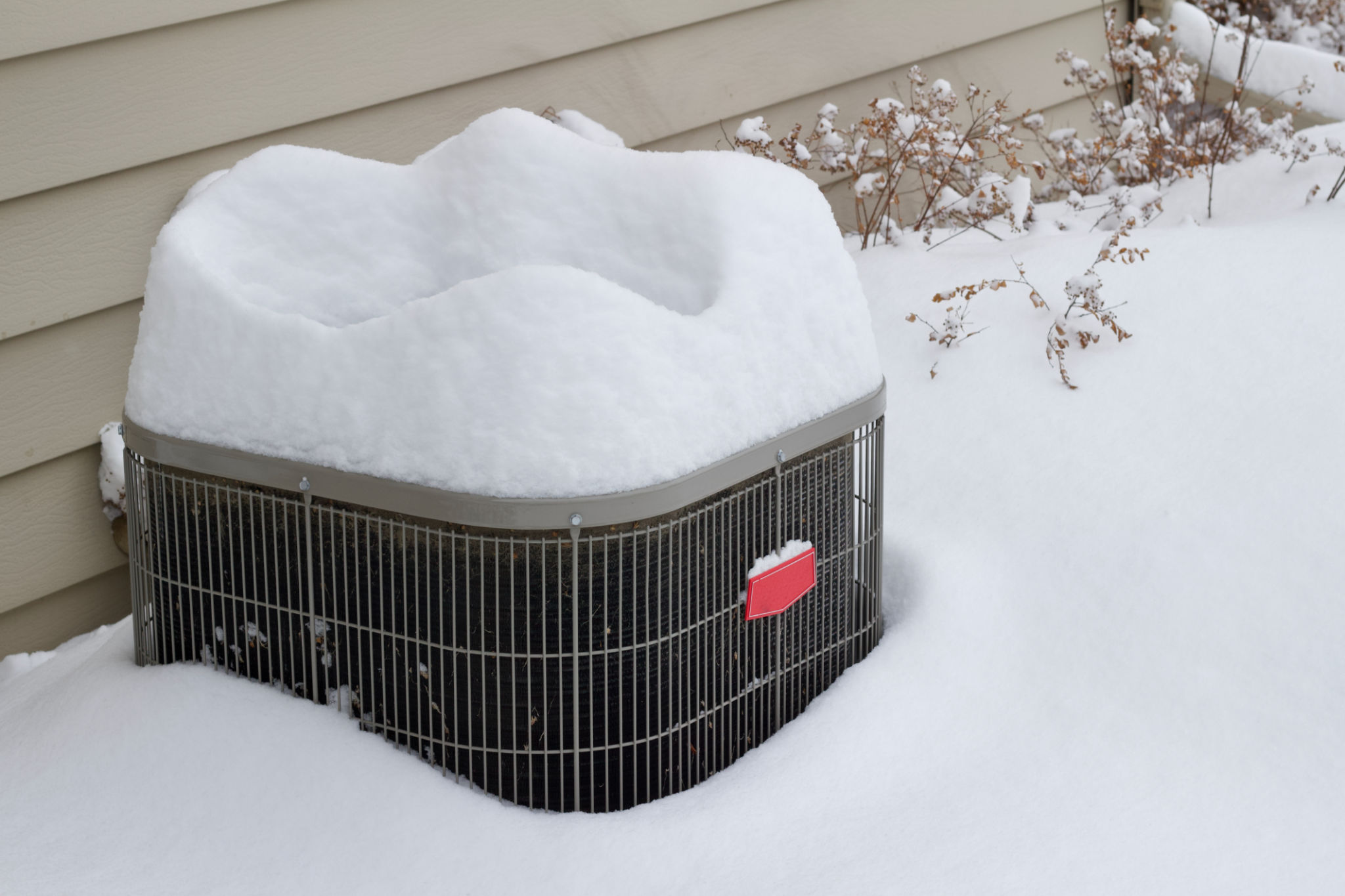 View of an exterior air conditioner unit covered with deep snow following a snow storm View of an exterior air conditioner unit covered with deep snow following a snow storm