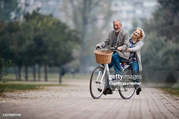 playful senior couple having fun on a bike in autumn day. - mature couple winter outdoors stock pictures, royalty-free photos & images