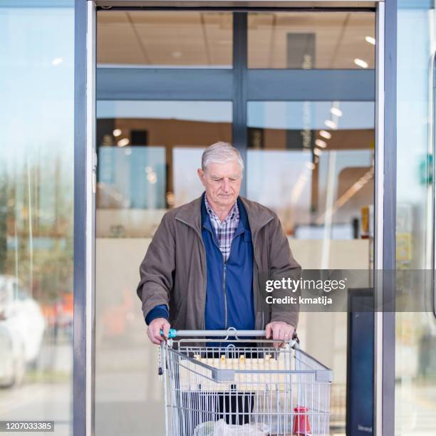 homme adulte aîné quittant le supermarché et poussant le chariot d’achat - automatic photos et images de collection