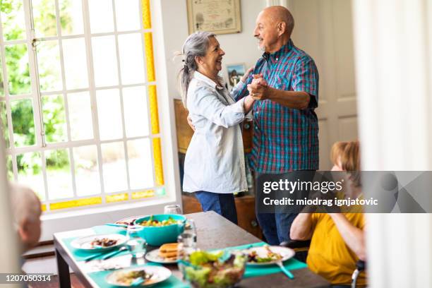 lovely senior couple dancing during lunch time with their friends at home - senior man dancing on table stock pictures, royalty-free photos & images