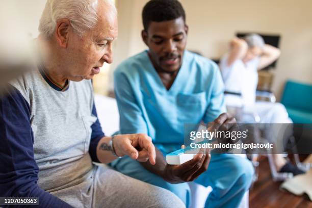 black male nurse giving instructions to senior patient when to take his pills - male at home imagens e fotografias de stock
