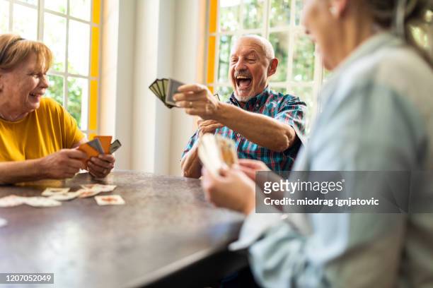 group of senior friends enjoying while playing cards at home - playing card stock pictures, royalty-free photos & images