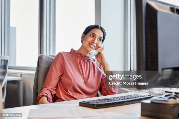 smiling businesswoman using telephone at desk - landline telephone stock pictures, royalty-free photos & images