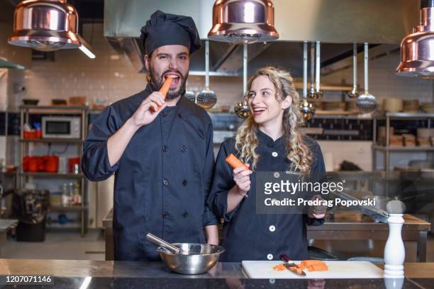 two happy service workers eating carrots in kitchen - accompagnement professionnel photos et images de collection