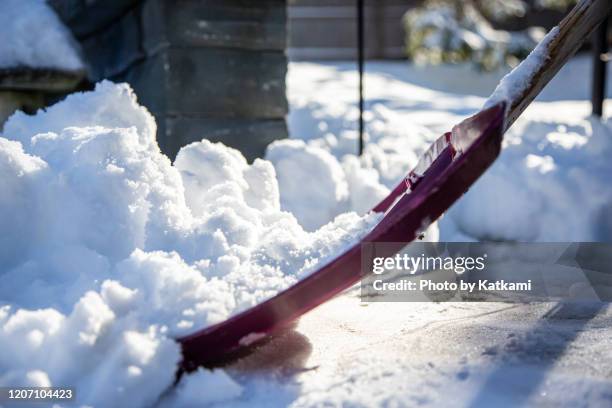 red shovel scooping snow off pavement - schneehaufen stock-fotos und bilder