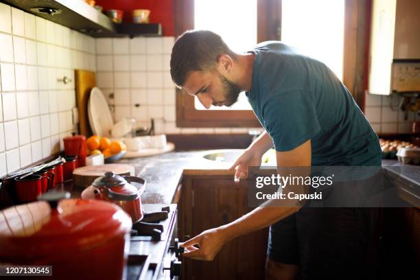 young man turning on the stove at kitchen - turn off light stock pictures, royalty-free photos & images