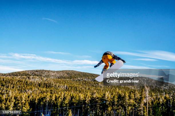 a young male snowboarder coming off a jump at a ski area in colorado on a sunny day - snowboard jump close up stock pictures, royalty-free photos & images