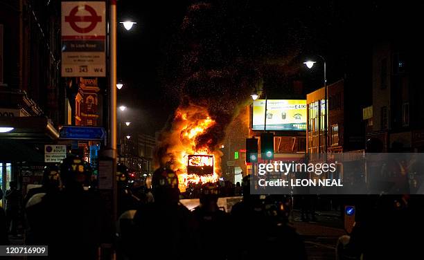 Double decker bus burns as riot police try to contain a large group of people on a main road in Tottenham, north London on August 6 2011. Two police...