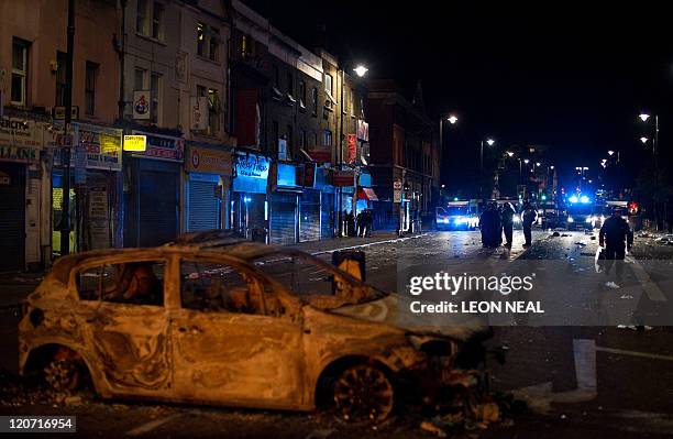 Burnt-out police car lays in the street as riot police try to contain a large group of people on a main road in Tottenham, north London on August 6...