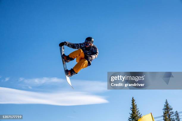 ein junger snowboarder, der an einem sonnigen tag in einem skigebiet in colorado von einem sprung abkommt - big air stock-fotos und bilder